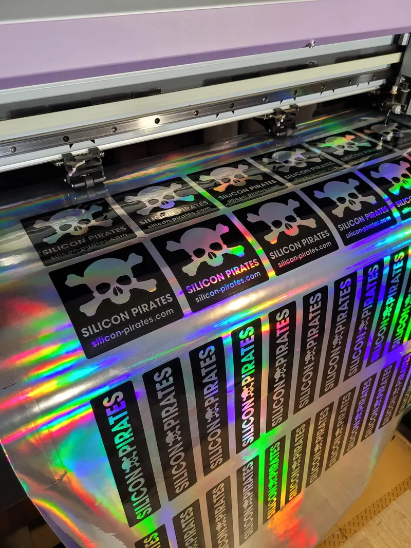 A sheet of holographic Silicon Pirates stickers on the vinyl plotter: skull stickers on top, name strips below