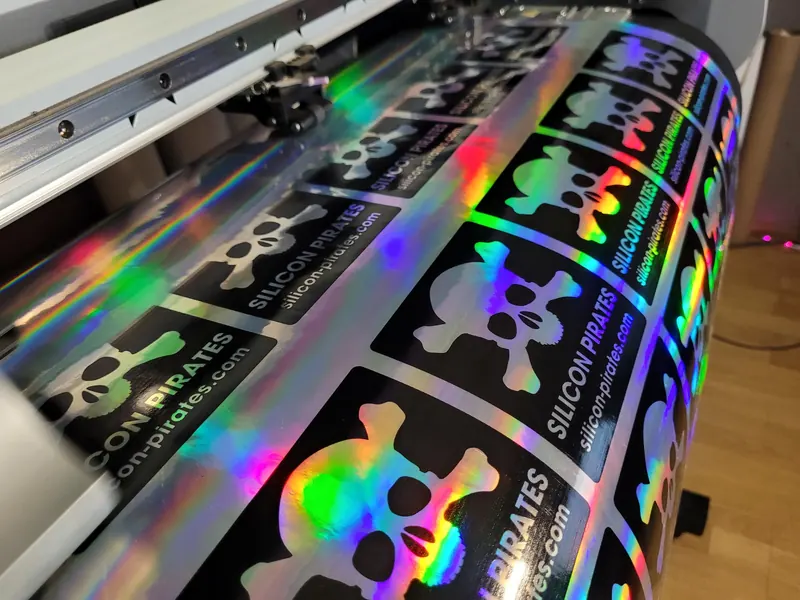 A row of holographic skull and crossbones stickers reading Silicon Pirates and silicon-pirates.com, curving over the plotter roller